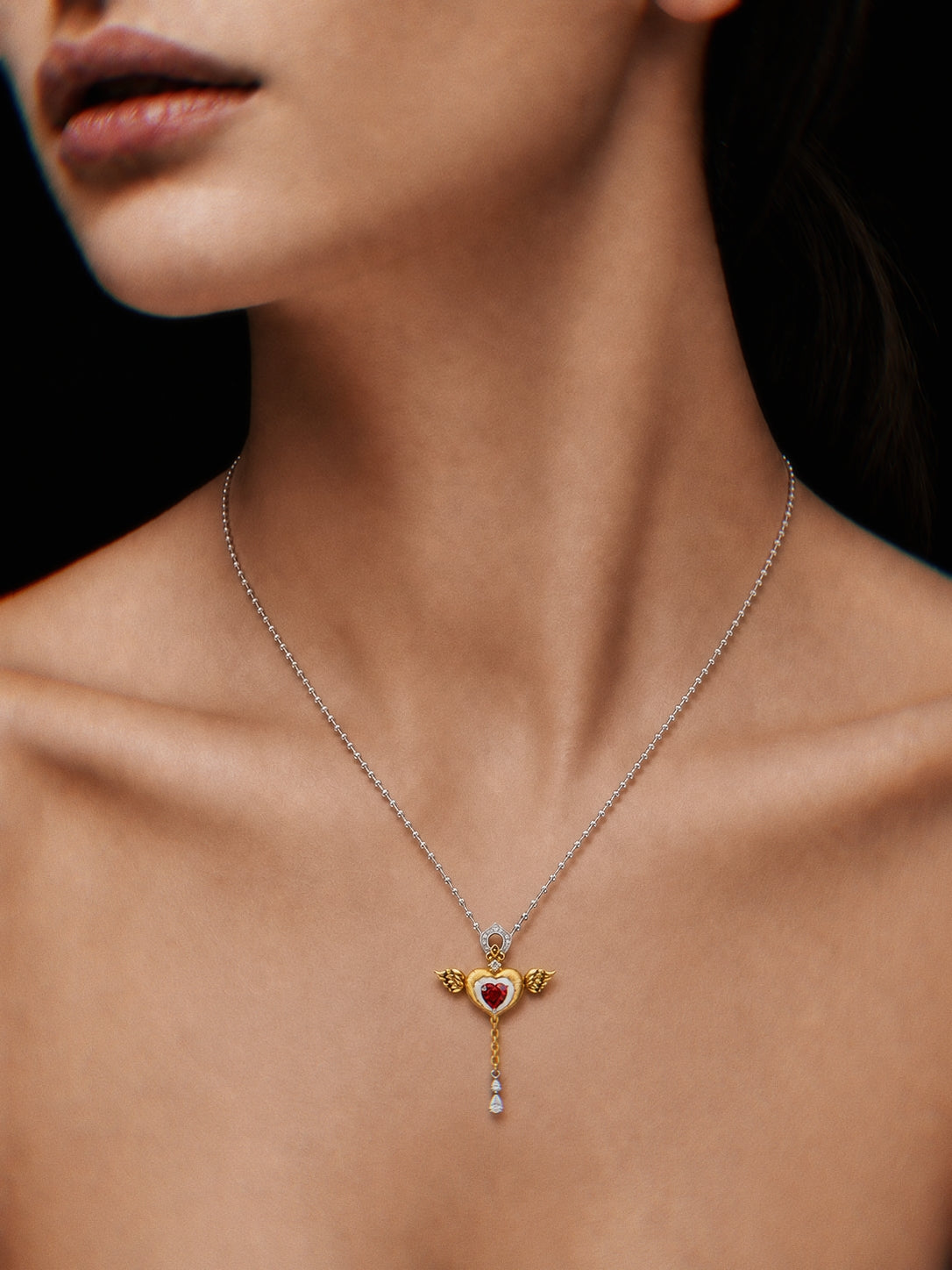 PurpleSea Heart Pendant, sterling silver heart pendant with red center stone, gold wing details and a dangling crystal drop, shown worn as a necklace on a model
