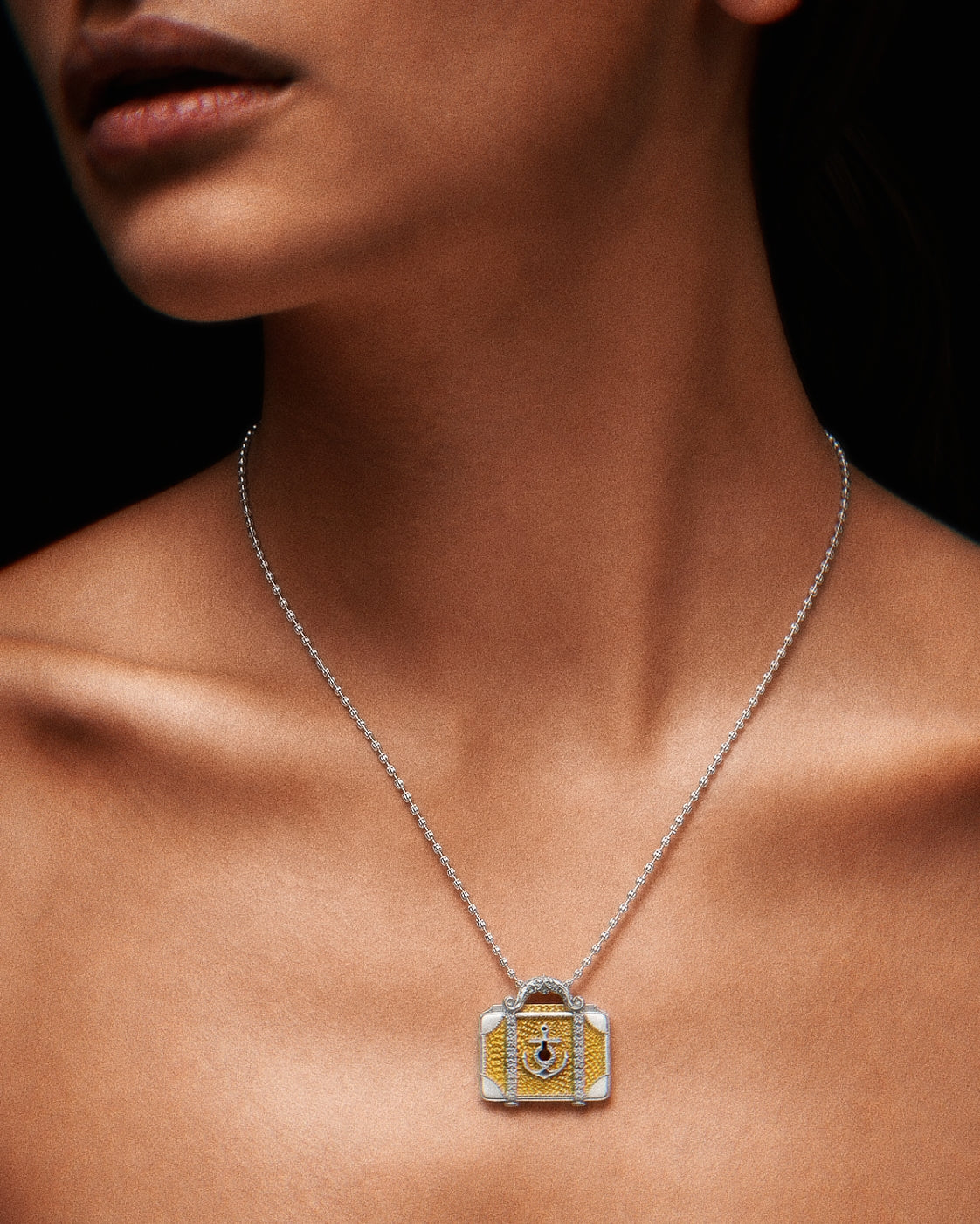 PurpleSea Suitcase Pendant, gold and silver-tone suitcase pendant with textured panels, corner details and a purple horseshoe-style emblem, shown worn as a necklace on a model