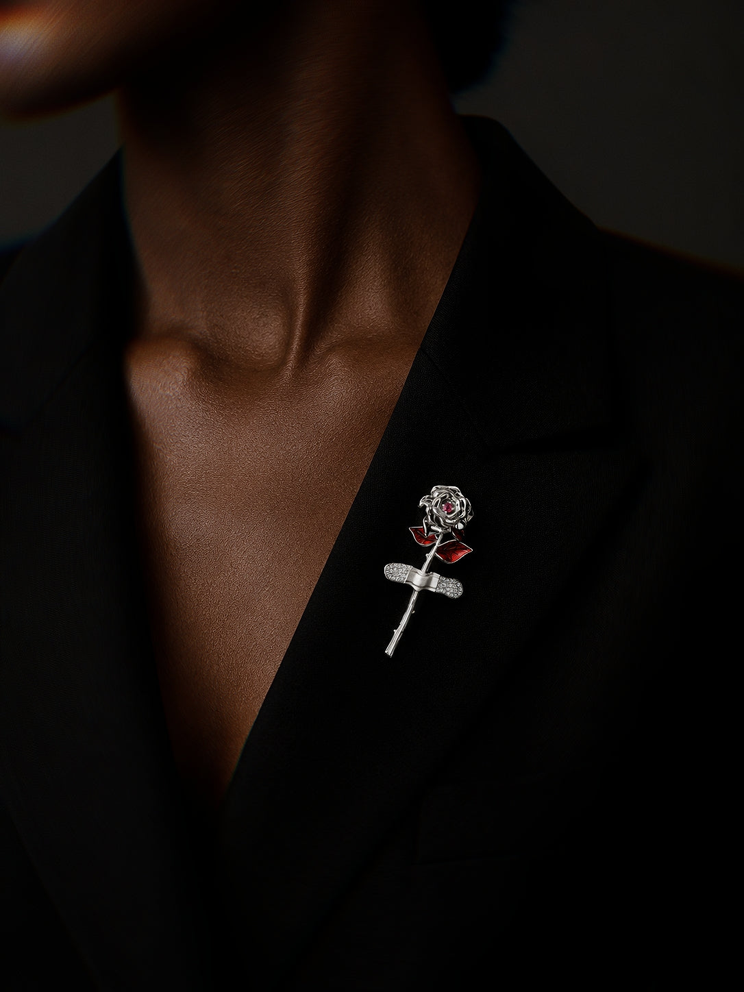 PurpleSea Rose Brooch, sterling silver rose brooch with sculptural petals, red enamel leaves and a crystal-accented stem, shown worn on a model's black blazer