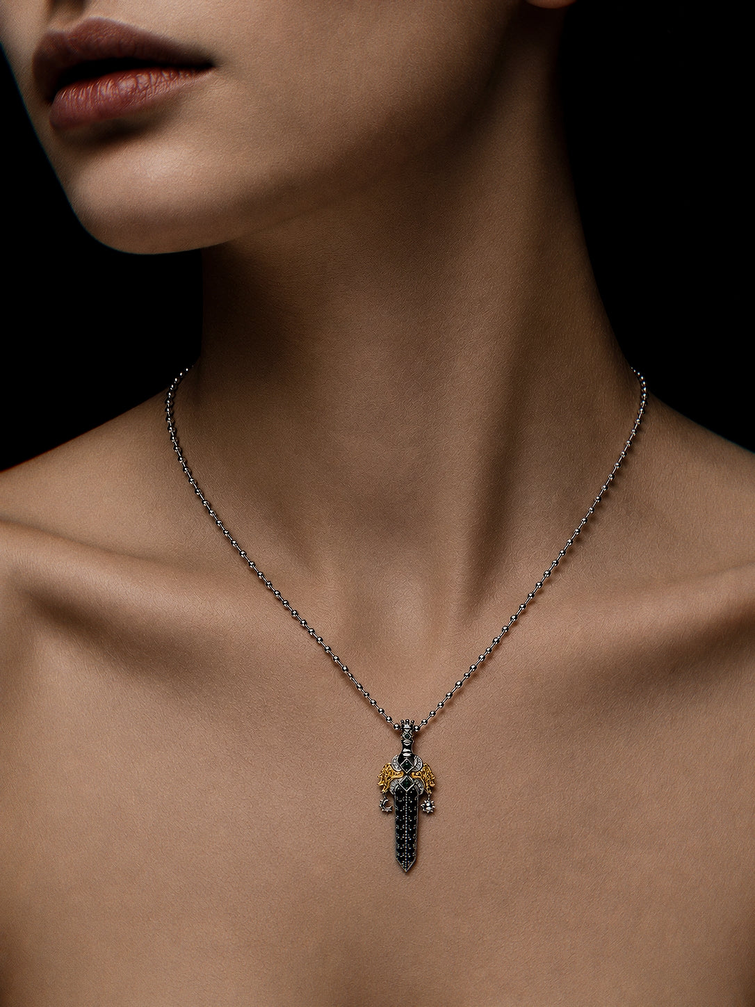 PurpleSea Judgment Sword Pendant, sterling silver sword pendant with black pavé-style detailing, gold wings and small blue accents, shown worn as a necklace on a model