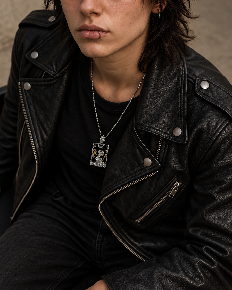A close-up lifestyle shot of a person wearing a black leather motorcycle jacket, black t-shirt, and a silver pendant necklace with a detailed portrait.